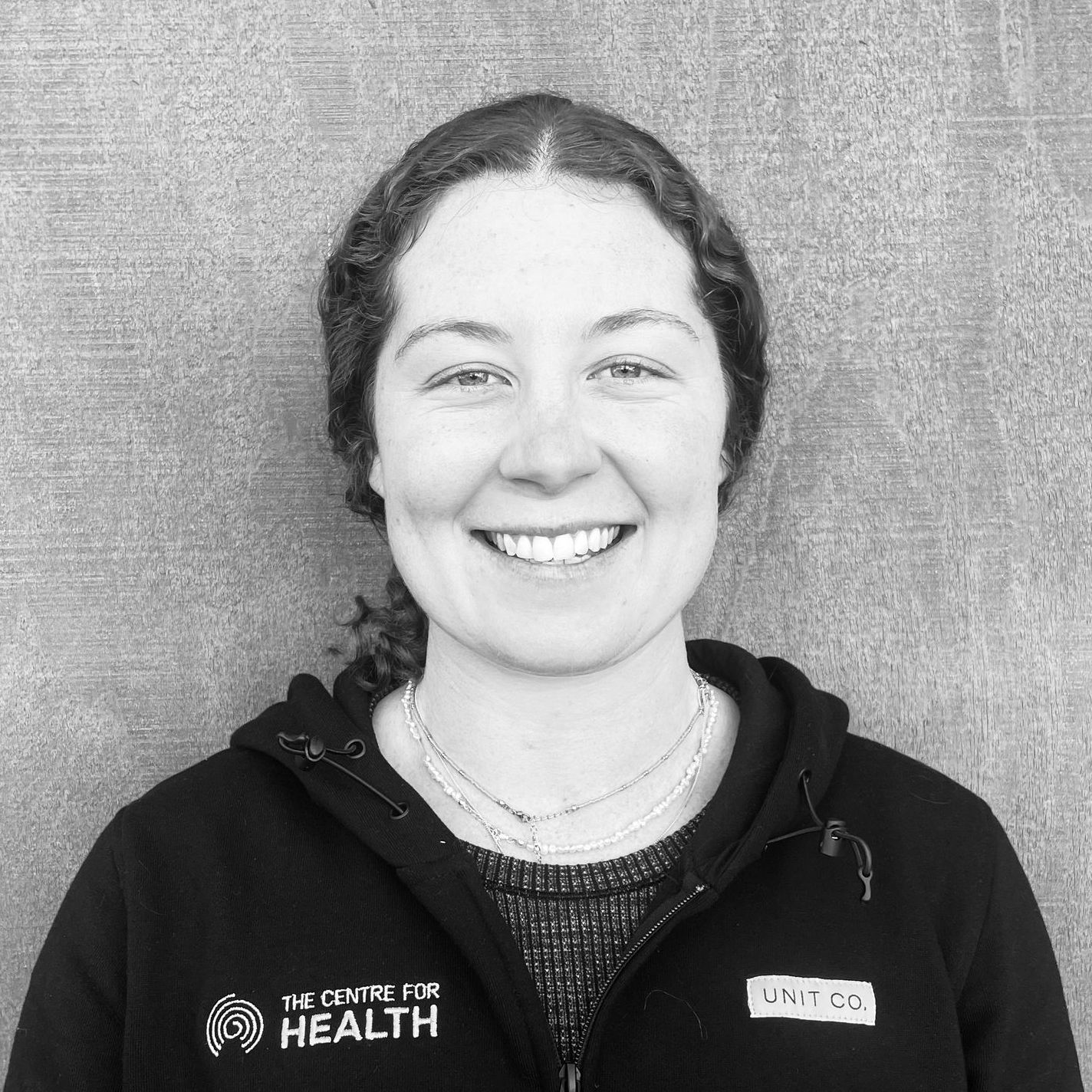 A woman is smiling in a black and white photo while wearing a hoodie.