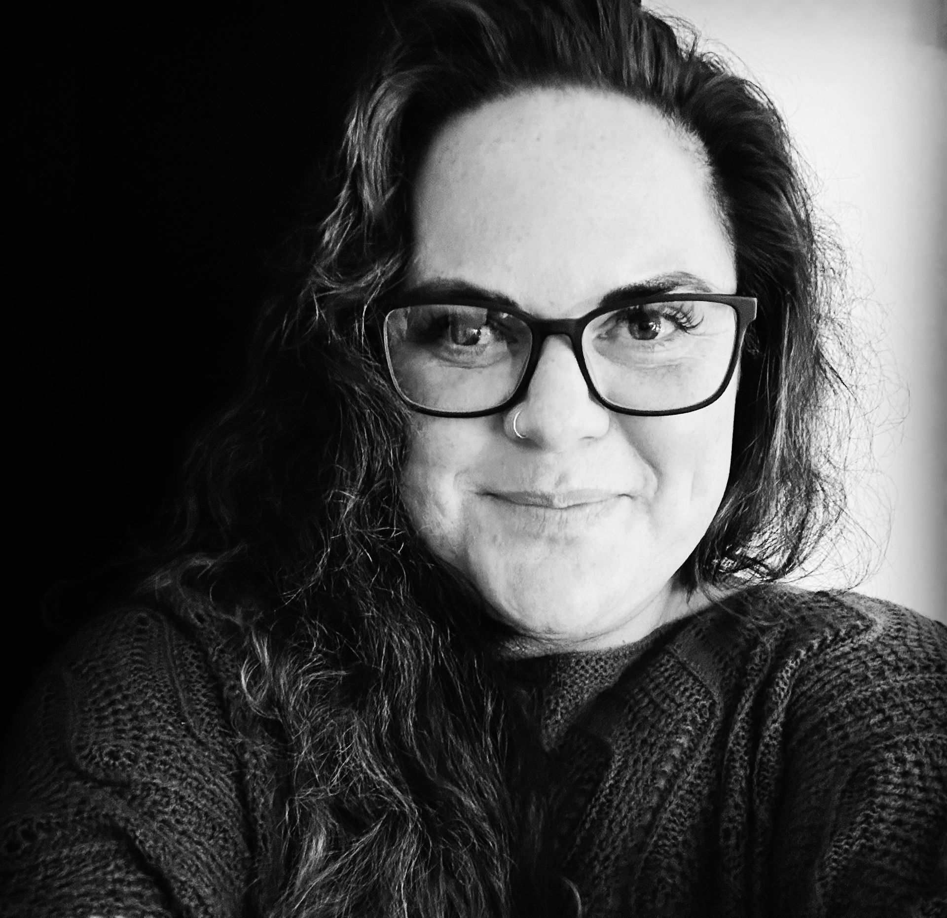 A woman wearing glasses and a black sweater is smiling in a black and white photo.