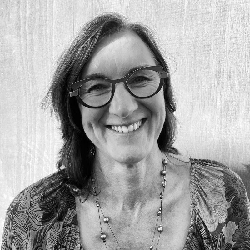A woman wearing glasses and a necklace is smiling in a black and white photo.