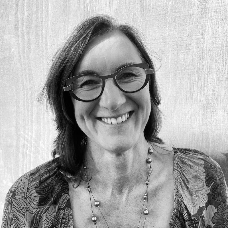 A woman wearing glasses and a necklace is smiling in a black and white photo.