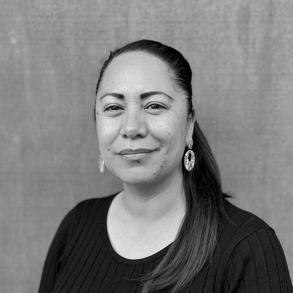 A woman wearing a black sweater and earrings is smiling in a black and white photo.