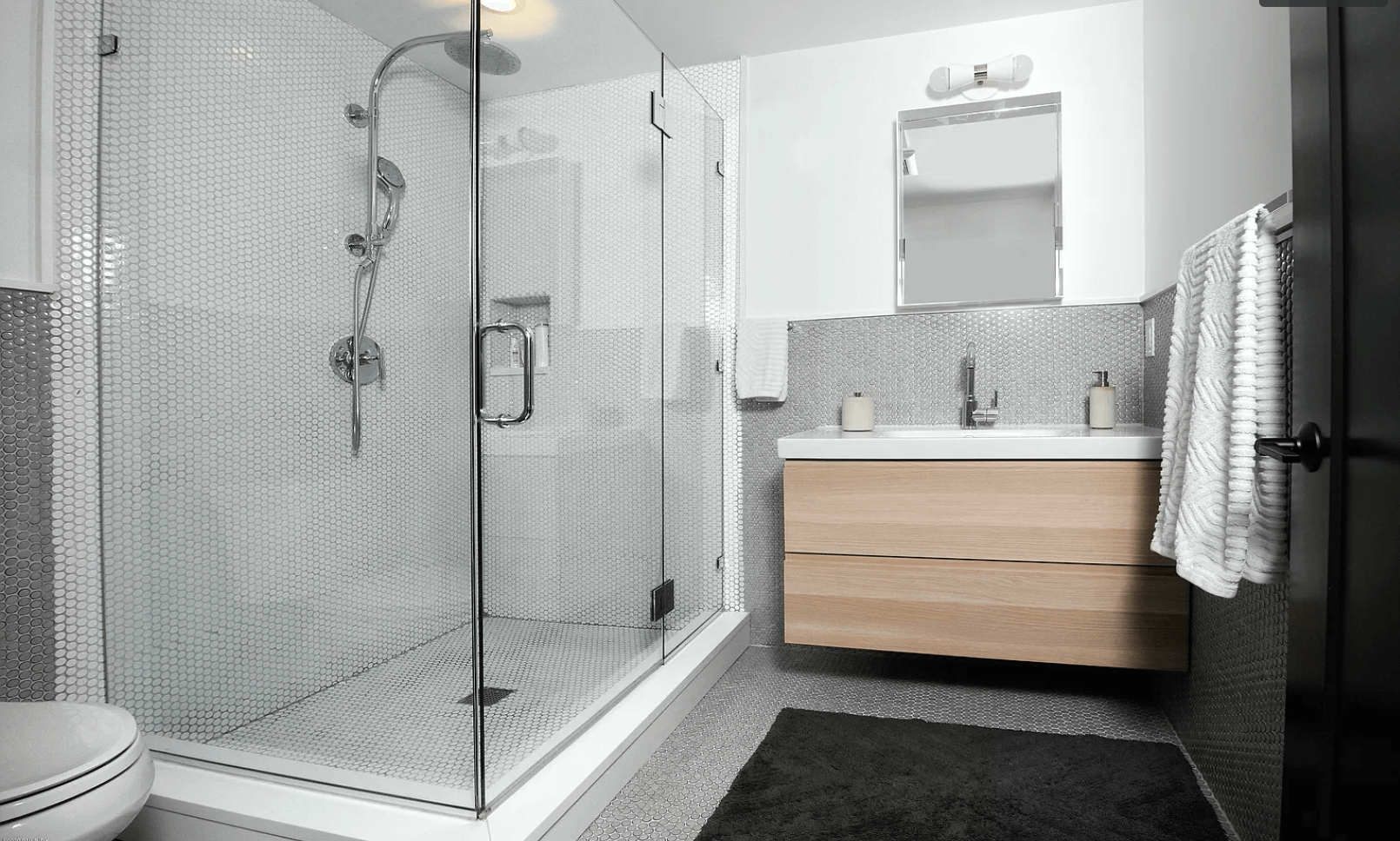 A bathroom with a walk in shower , sink , toilet and mirror.