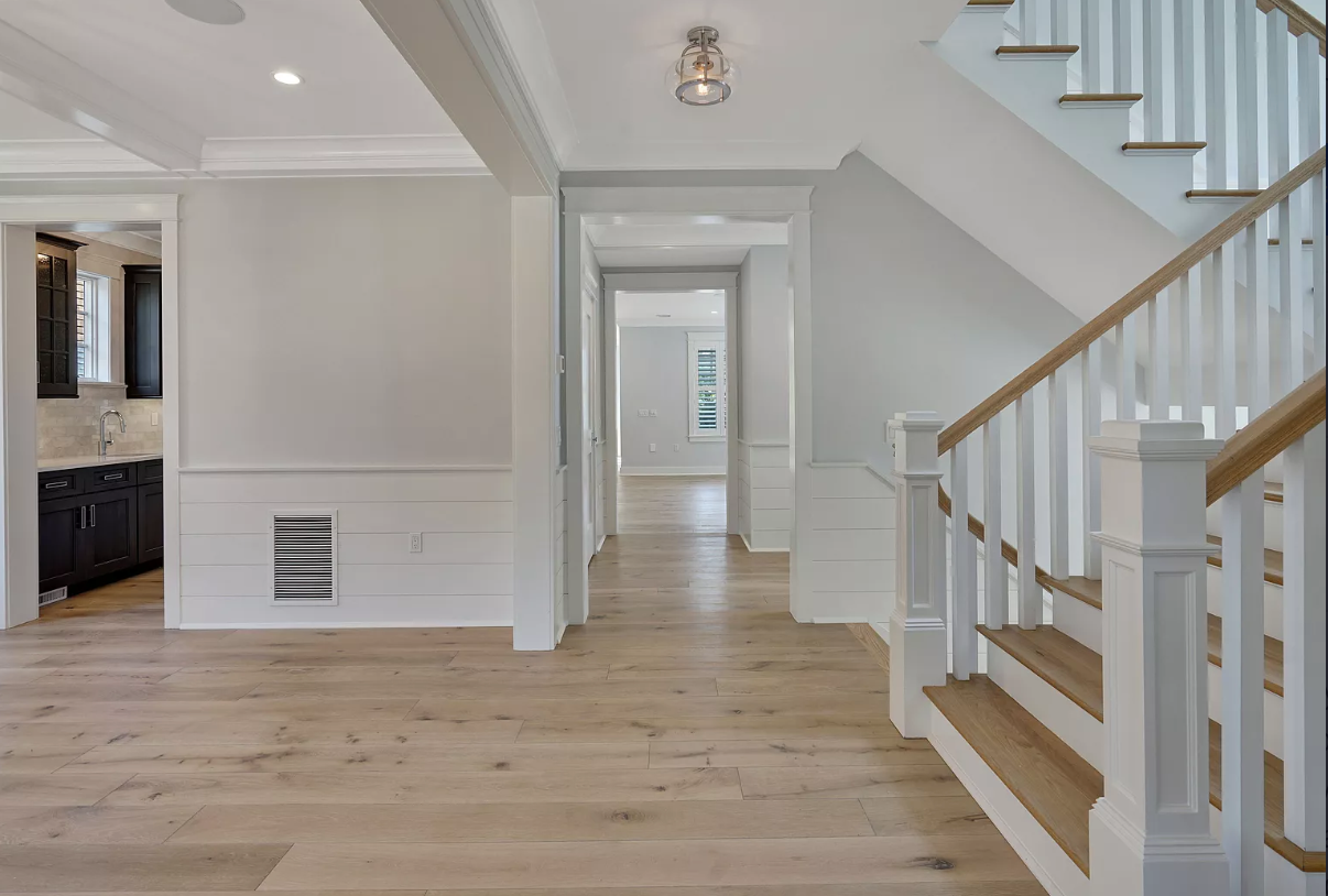 A hallway with wooden floors and stairs in a house.