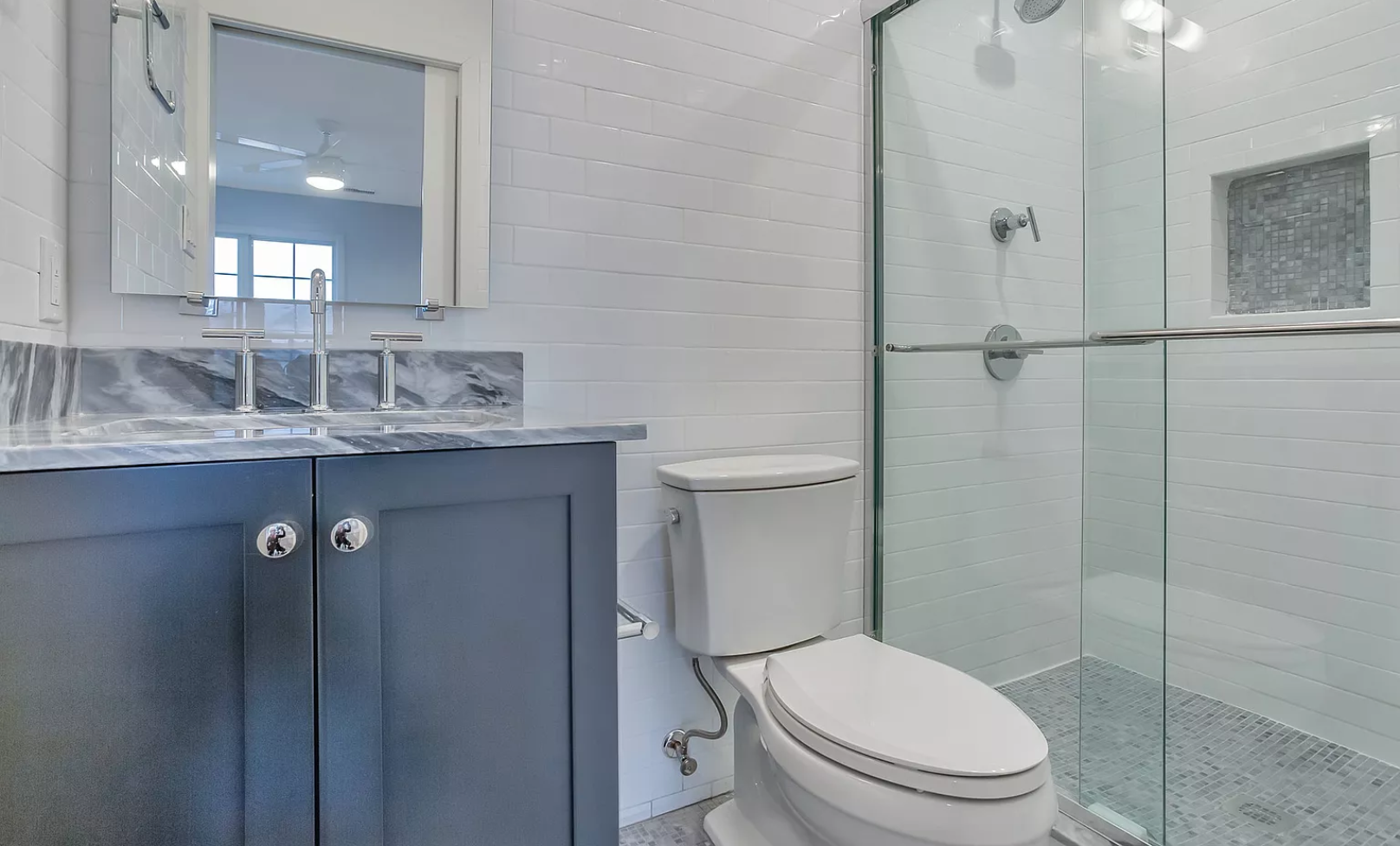 A bathroom with a toilet , sink , mirror and walk in shower.