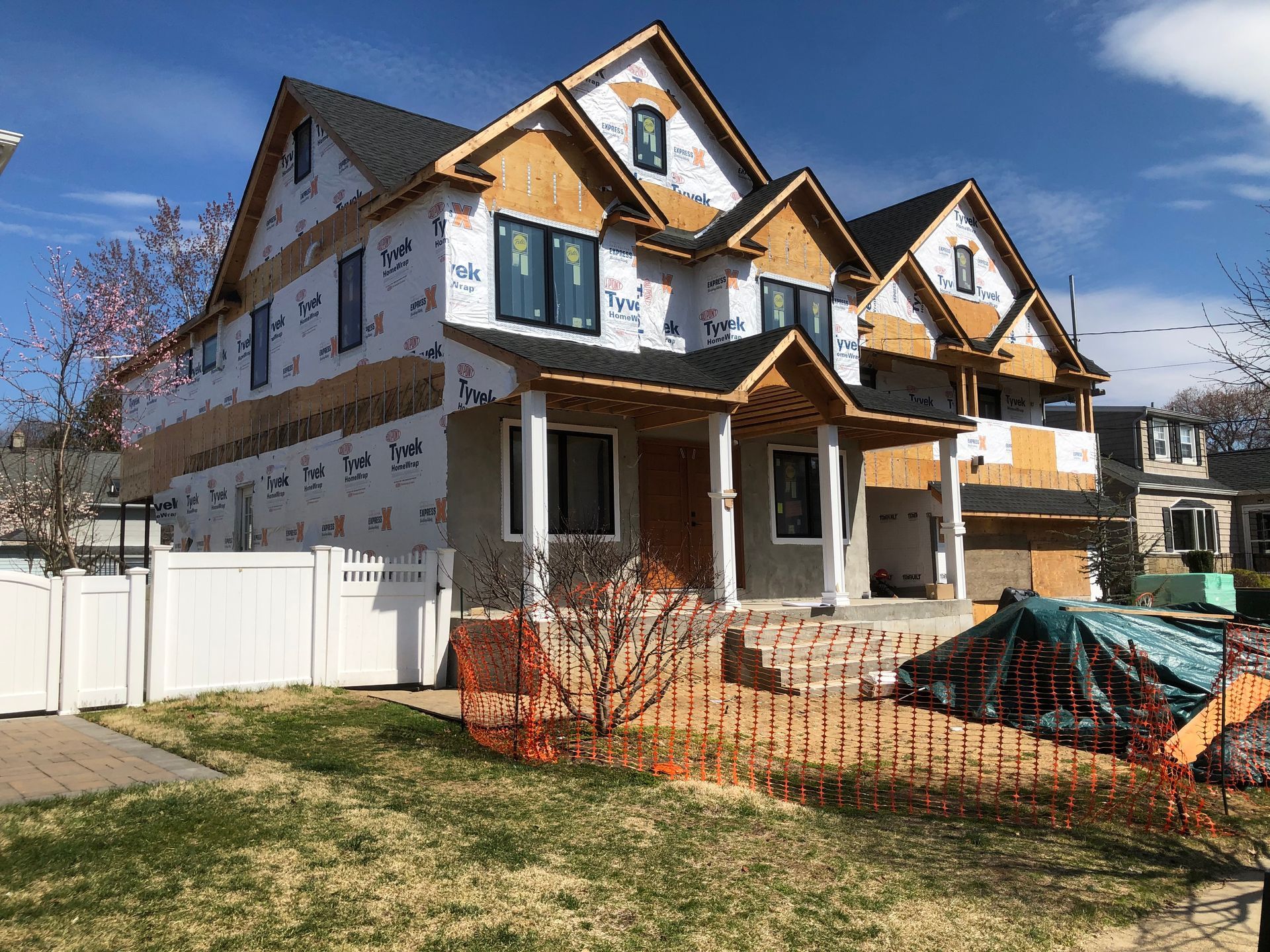 A large house under construction with a white fence in front of it.