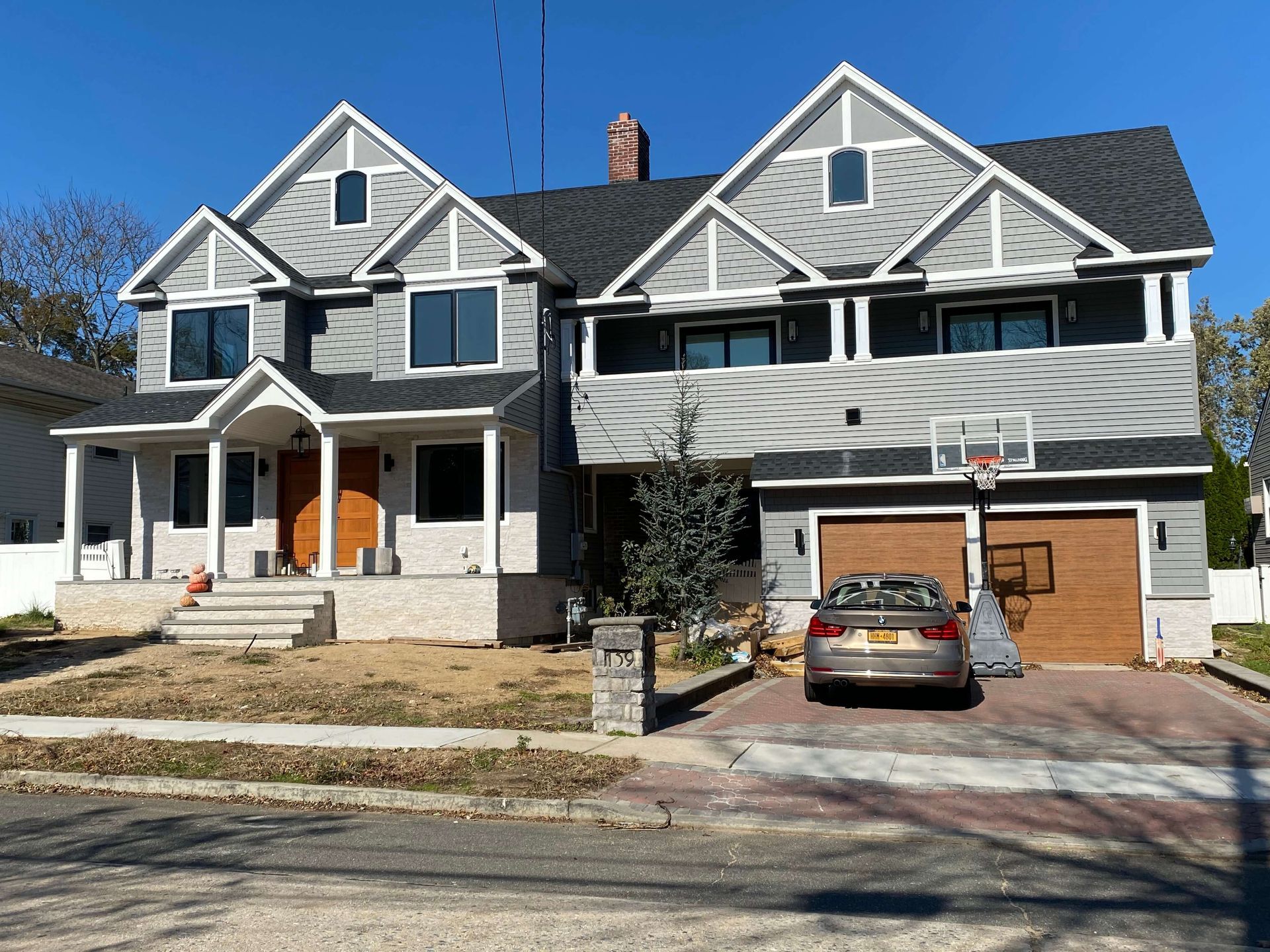 A car is parked in front of a house with a basketball hoop.