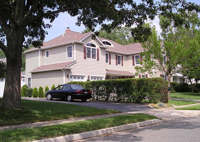 A black car is parked in front of a large house