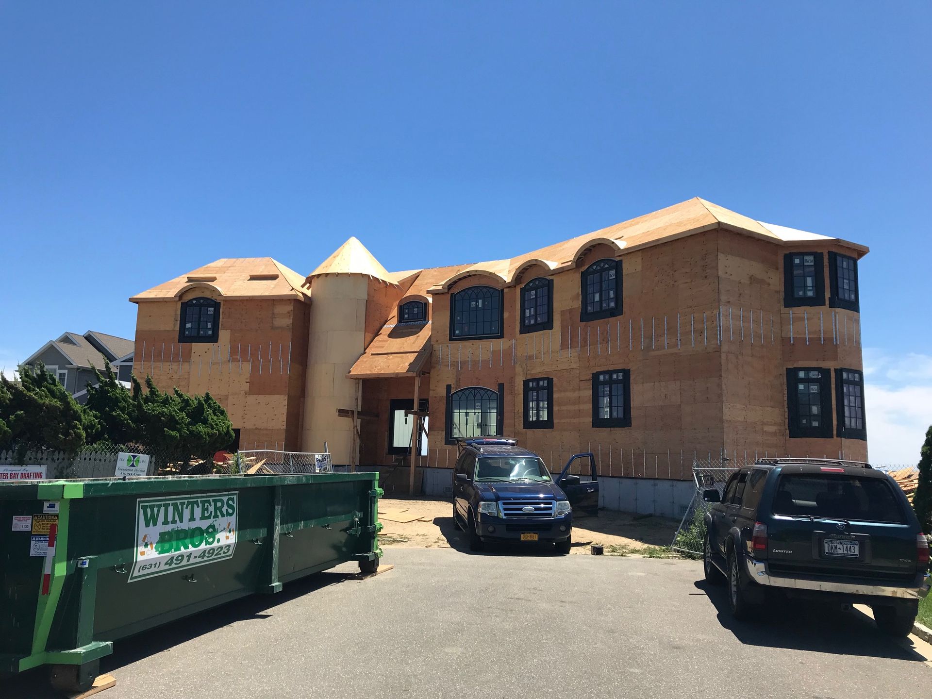 A large house under construction with a green dumpster in front of it