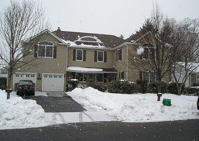 A car is parked in front of a house that is covered in snow