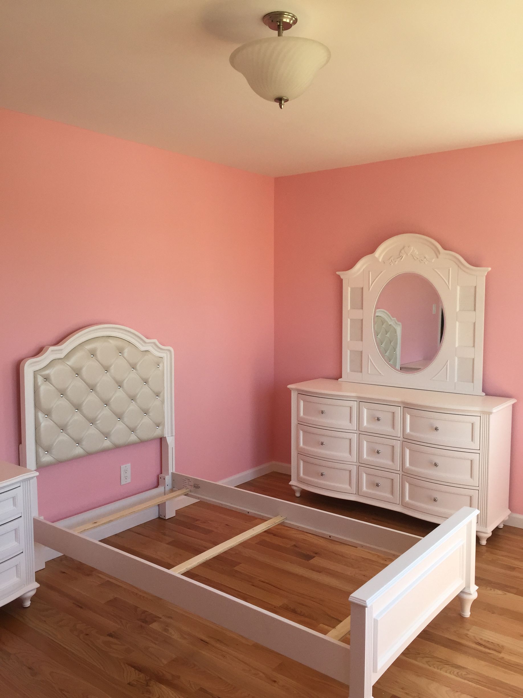 A bedroom with pink walls , a bed , dresser and mirror.