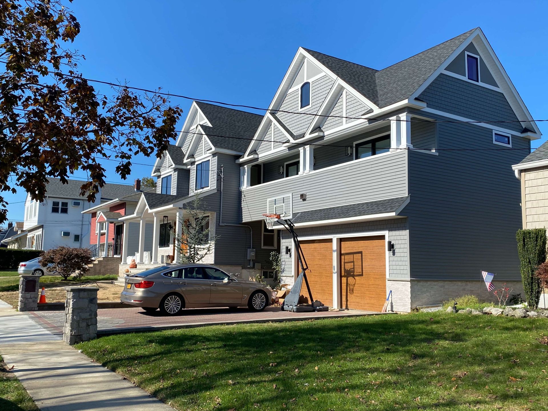 A car is parked in front of a large house with a basketball hoop.