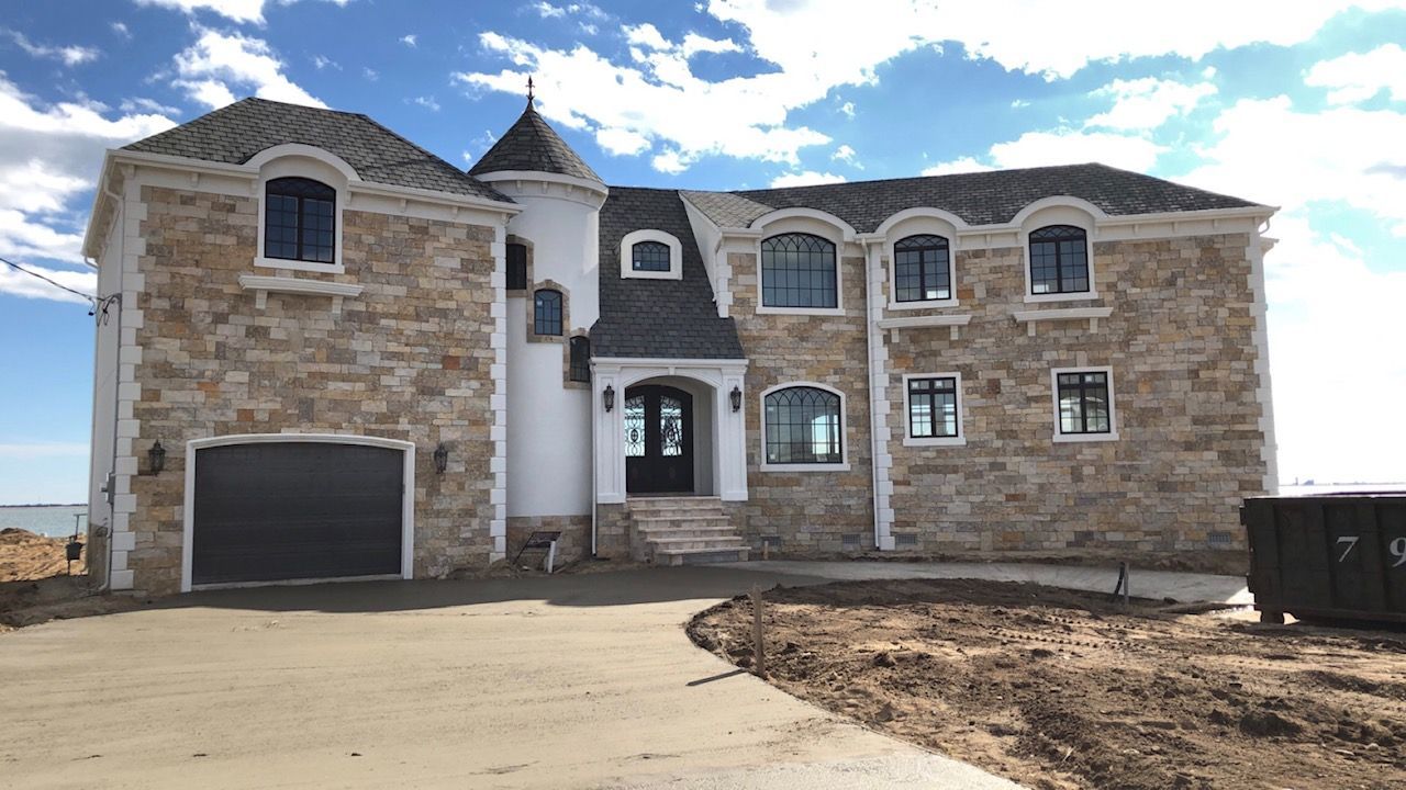 A large stone house with a black garage door is under construction.