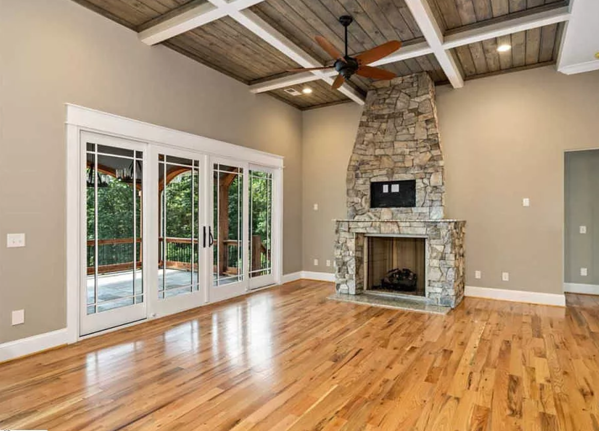 An empty living room with hardwood floors and a stone fireplace.