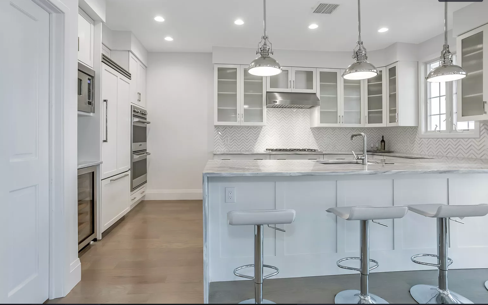 A kitchen with white cabinets and stools and a large island.