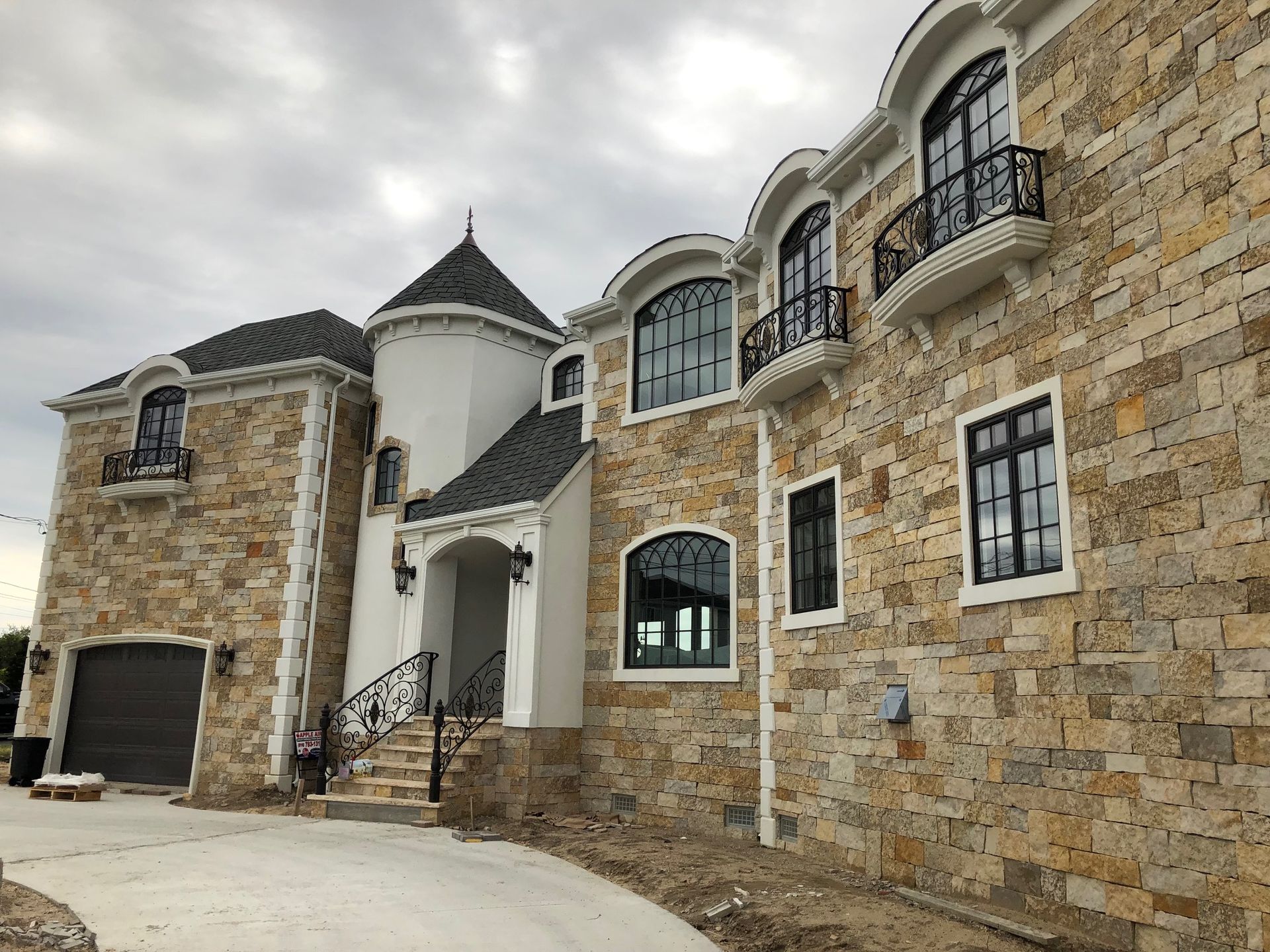 A large stone house with a balcony and stairs is being built.