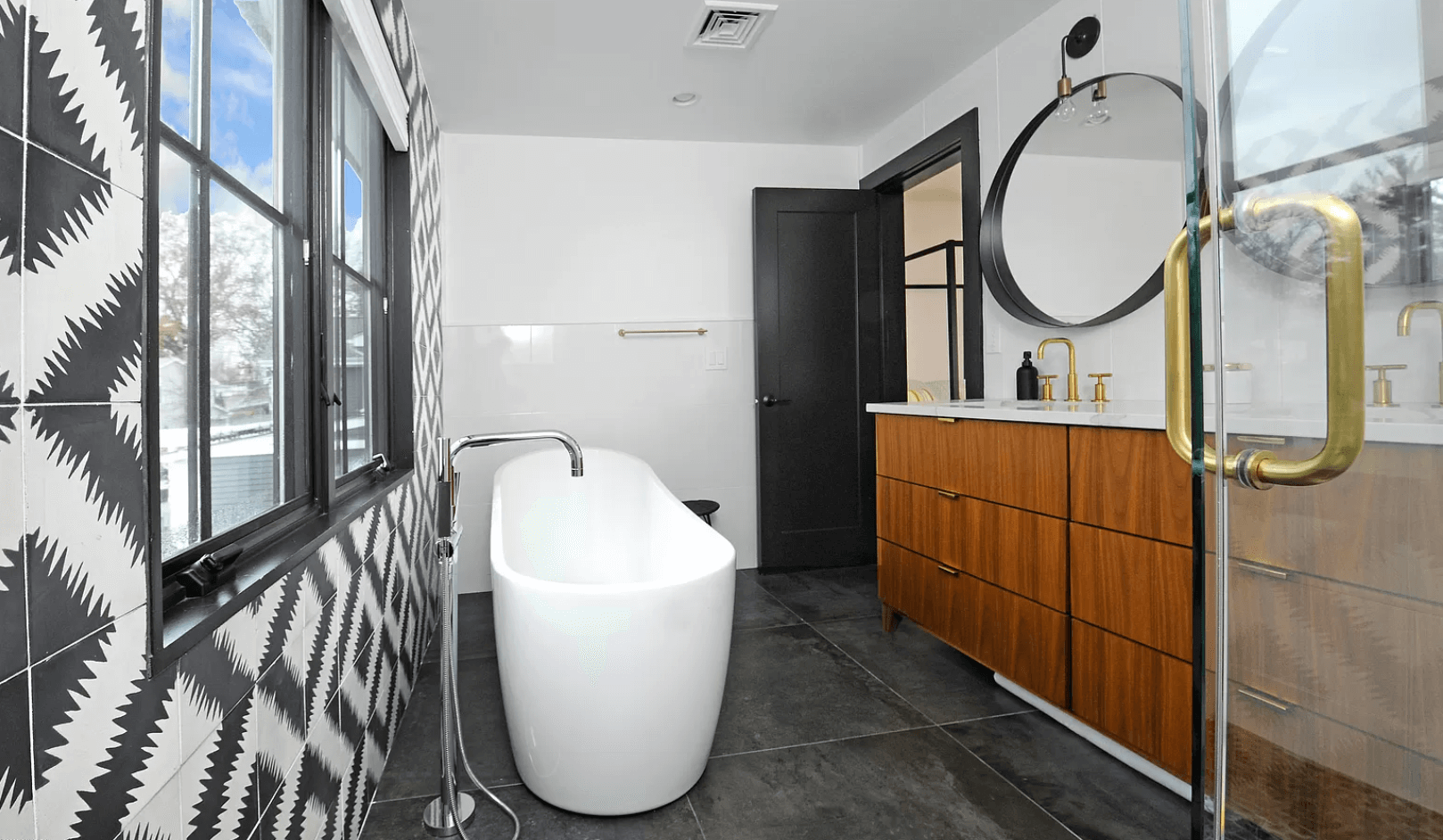 A bathroom with a bathtub , sink , mirror and window.