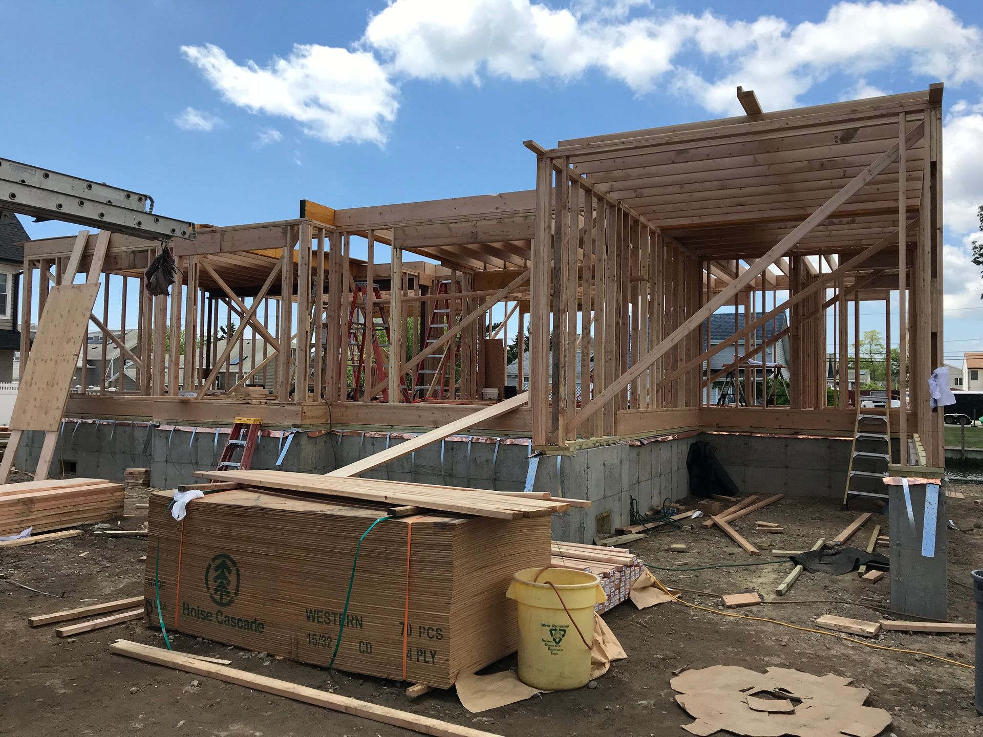A house is being built with a yellow bucket in front of it.