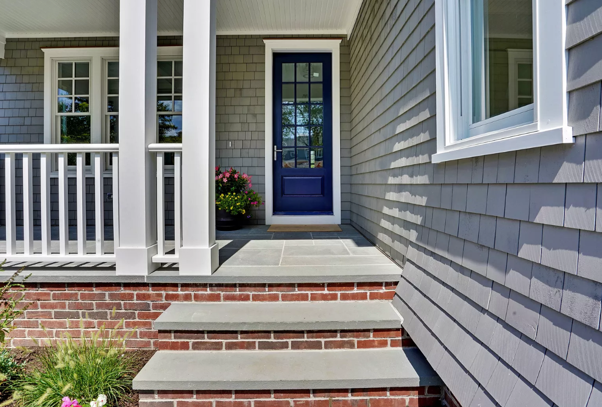 The front porch of a house with a blue door and stairs leading up to it.