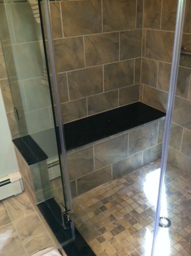 A bathroom with a walk in shower with a black bench.