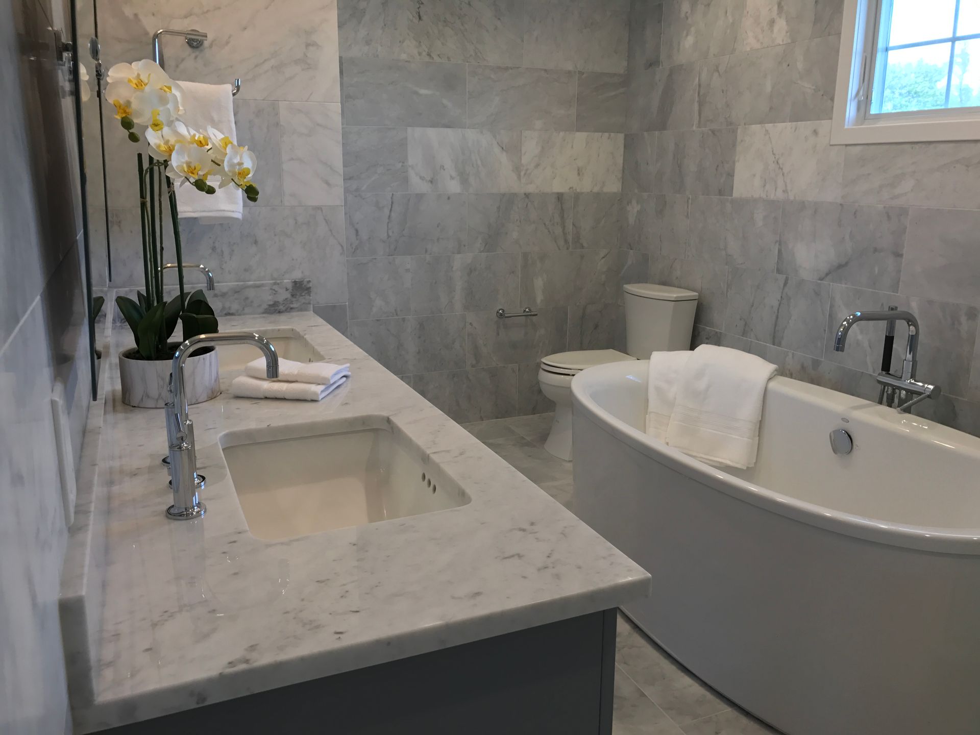 A bathroom with two sinks , a tub , a toilet and a window.