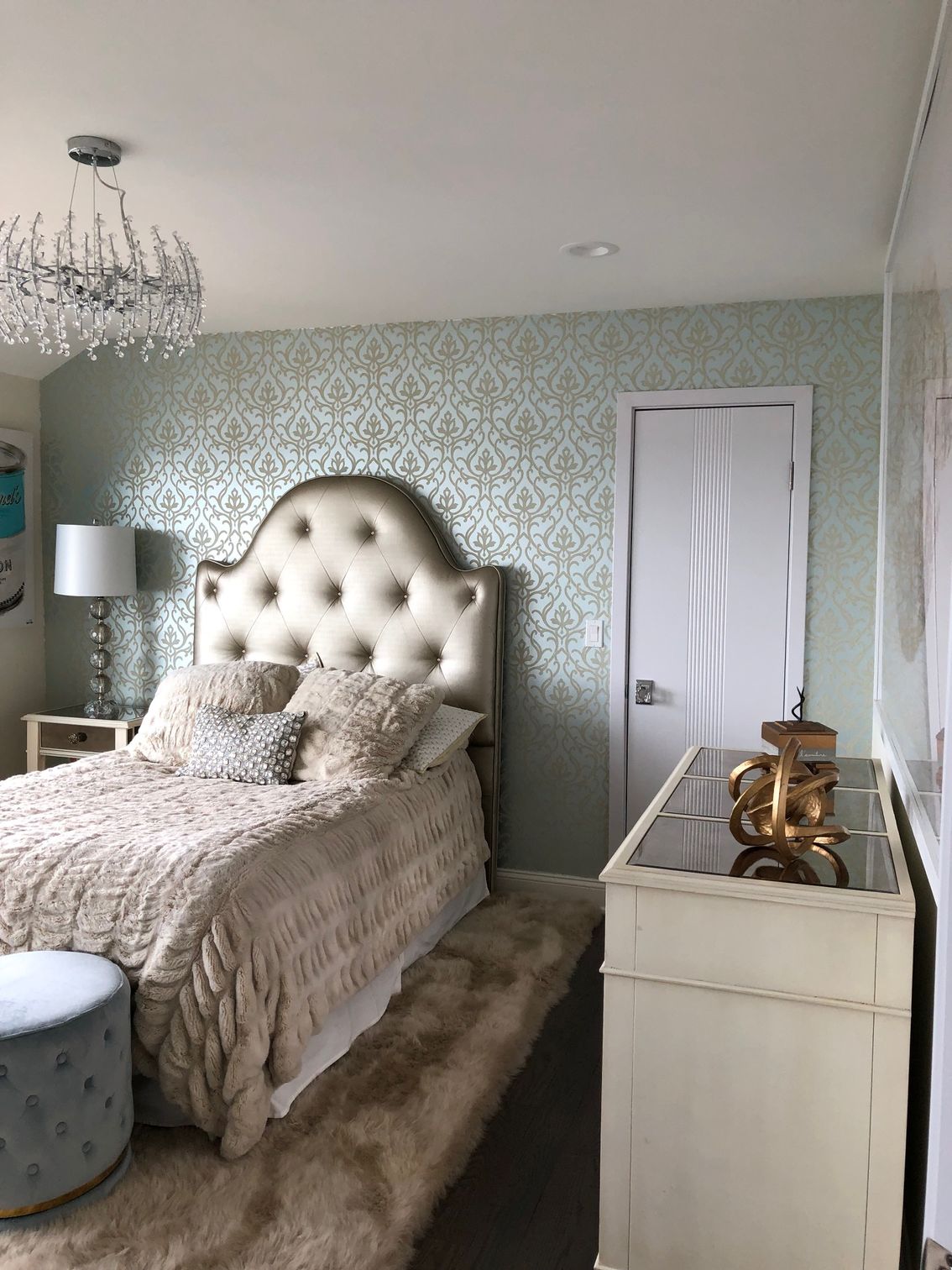 A bedroom with a bed , dresser , and chandelier.