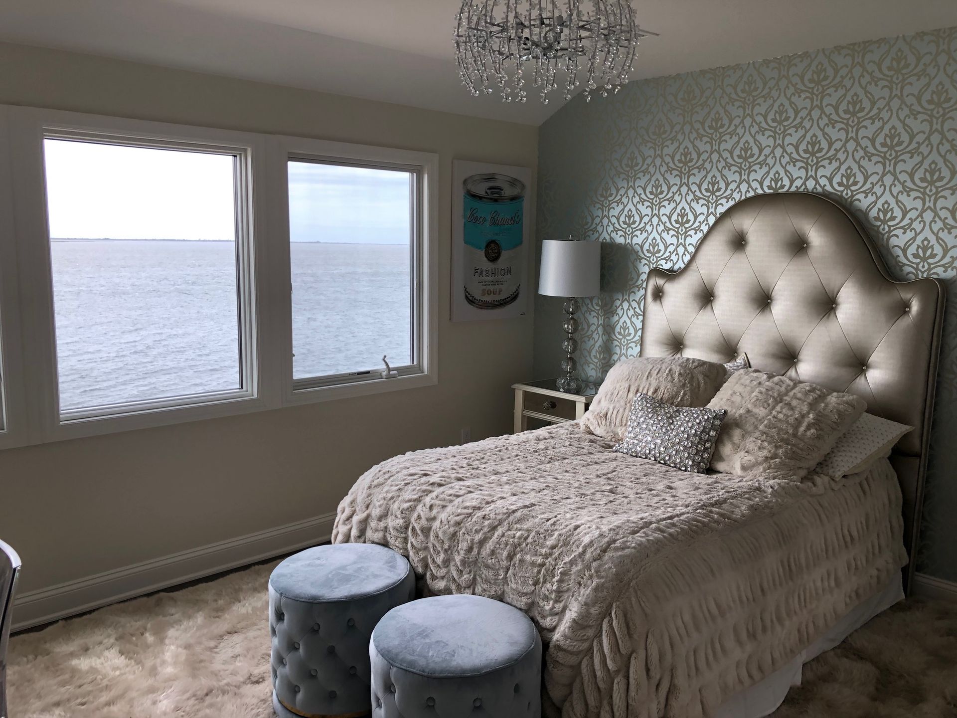 A bedroom with a bed , two ottomans , two windows and a view of the ocean.