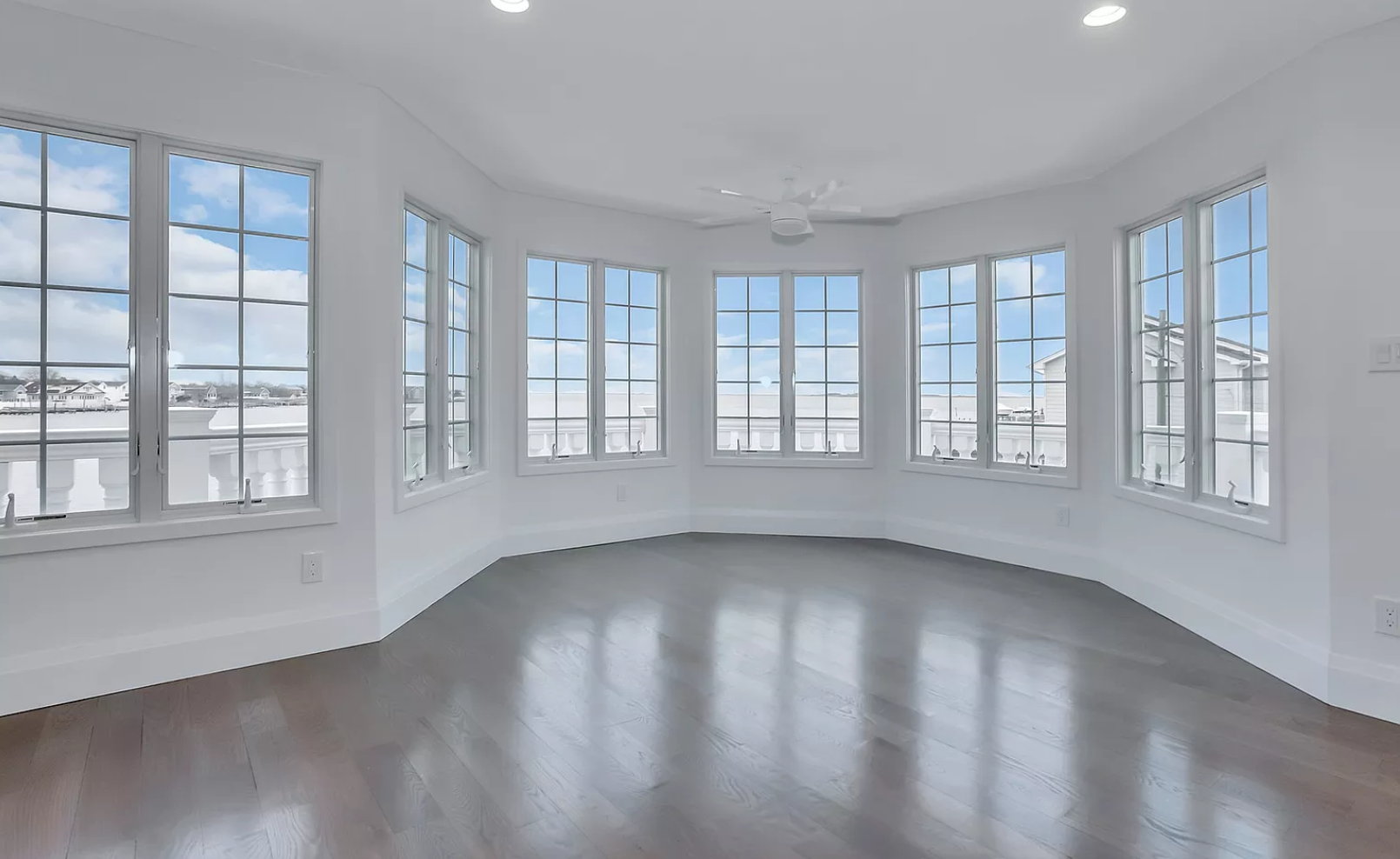 An empty room with a lot of windows and a ceiling fan.