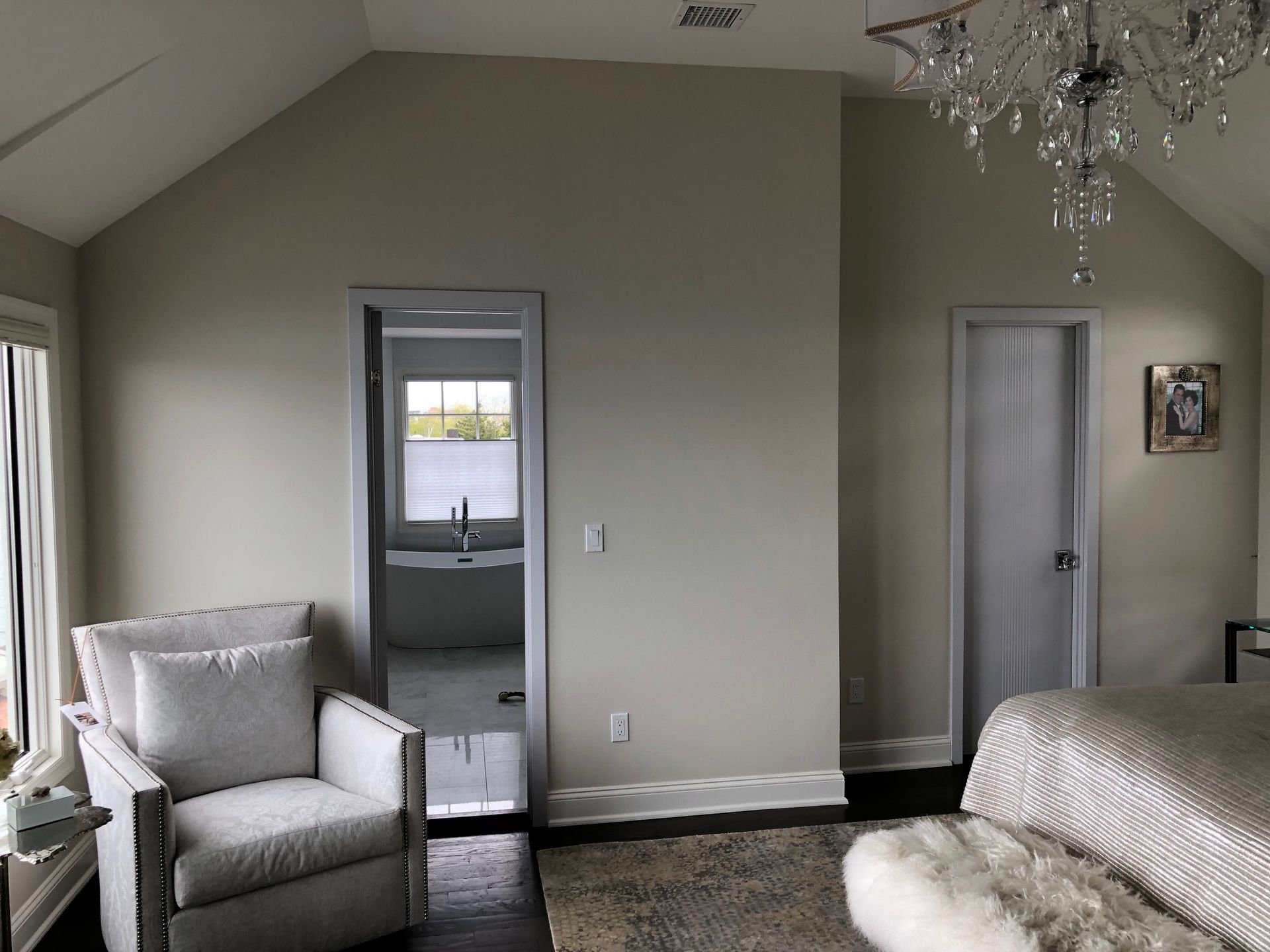 A bedroom with a chair a bed and a chandelier