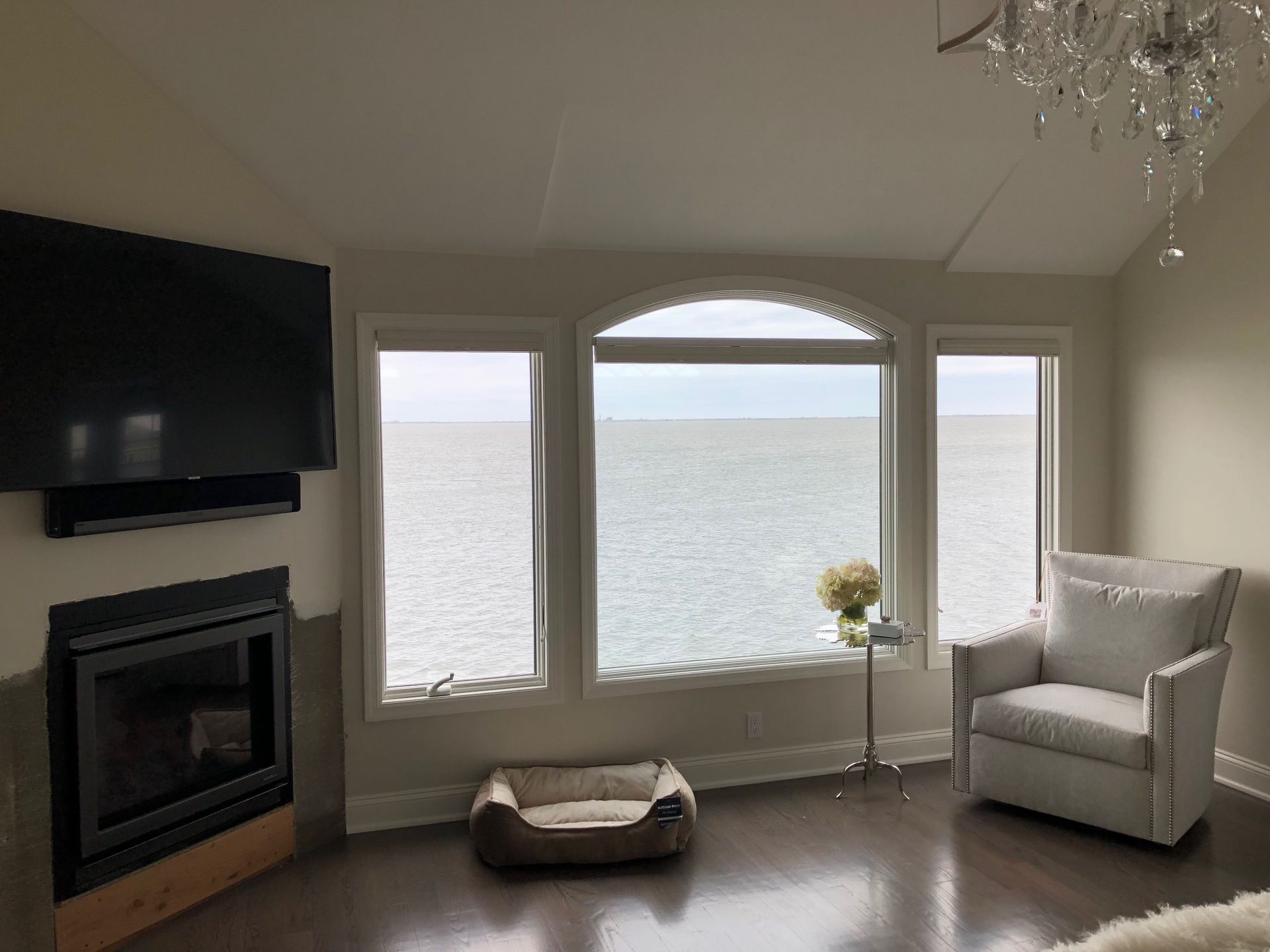 A living room with a fireplace , chair , television and a view of the ocean.
