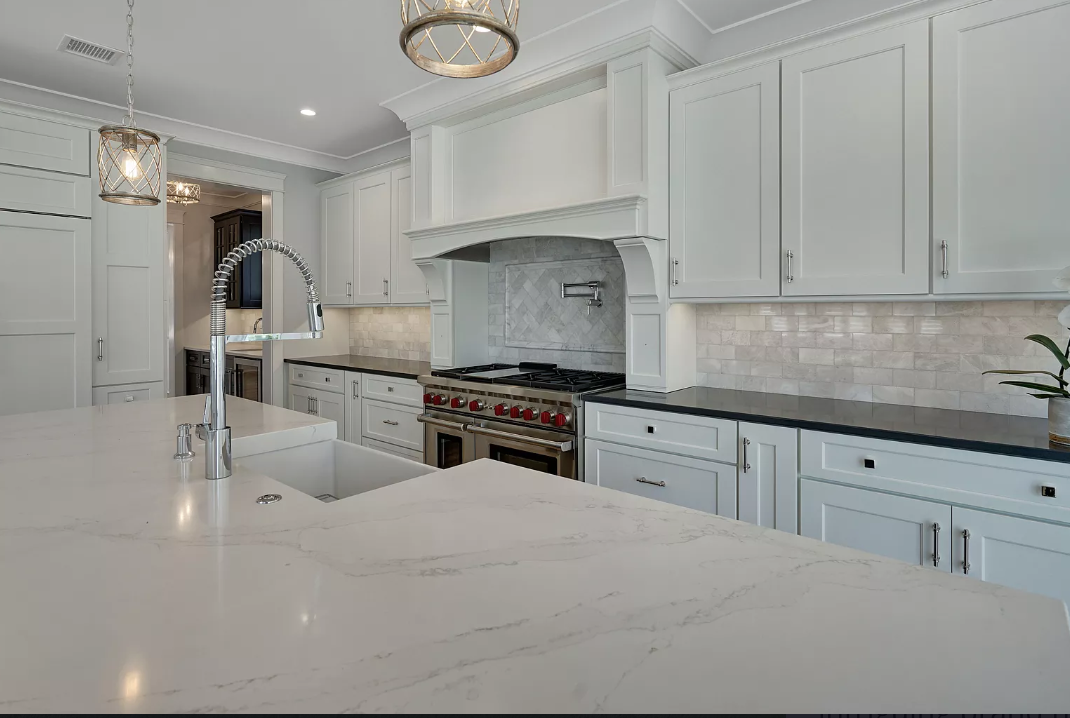 A kitchen with white cabinets , a stove , a sink , and a large island.