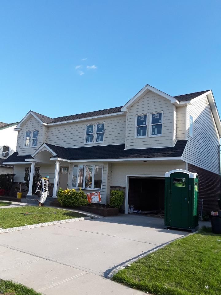 A large white house with a green portable toilet in front of it.