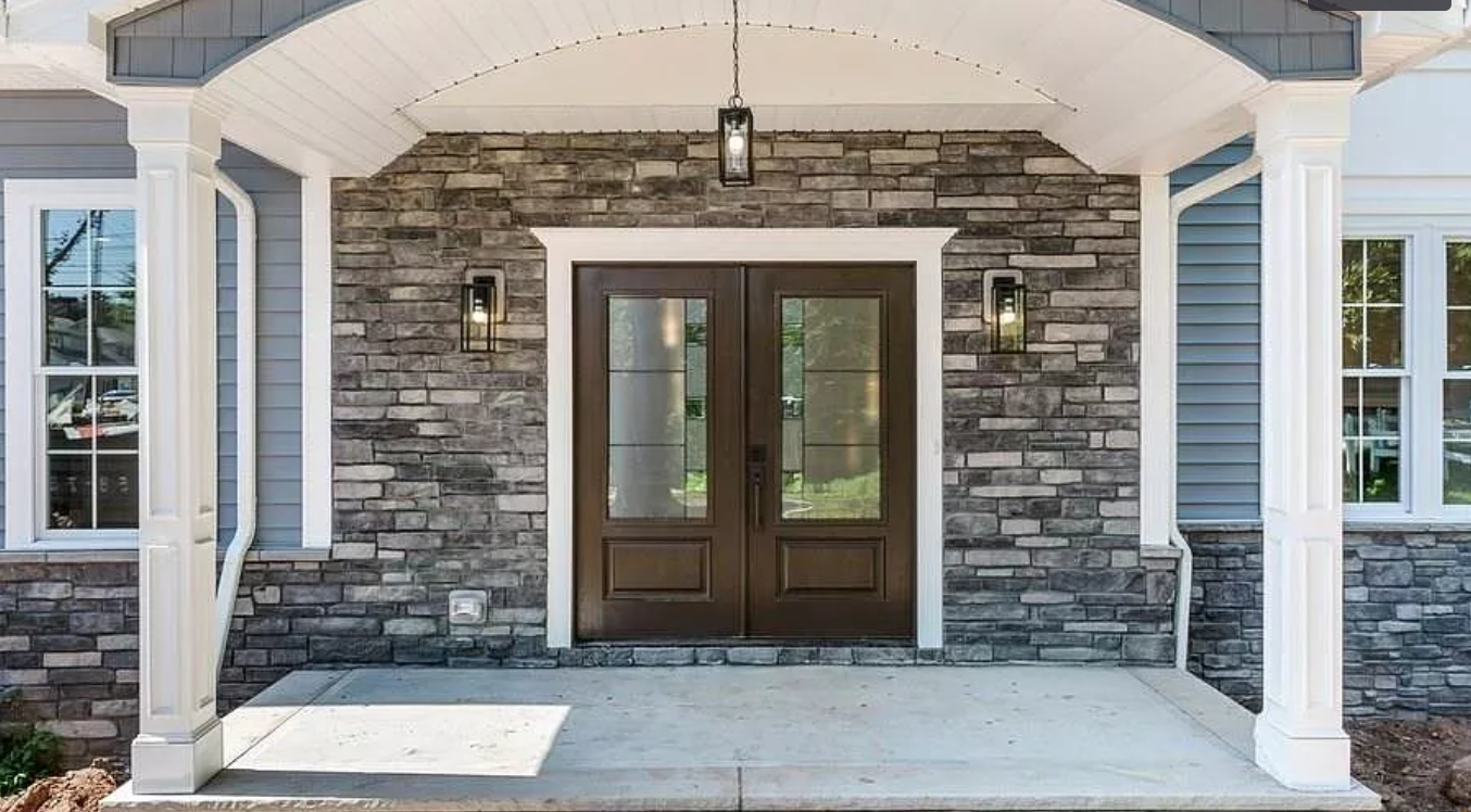 The front door of a house with a stone wall and a porch.