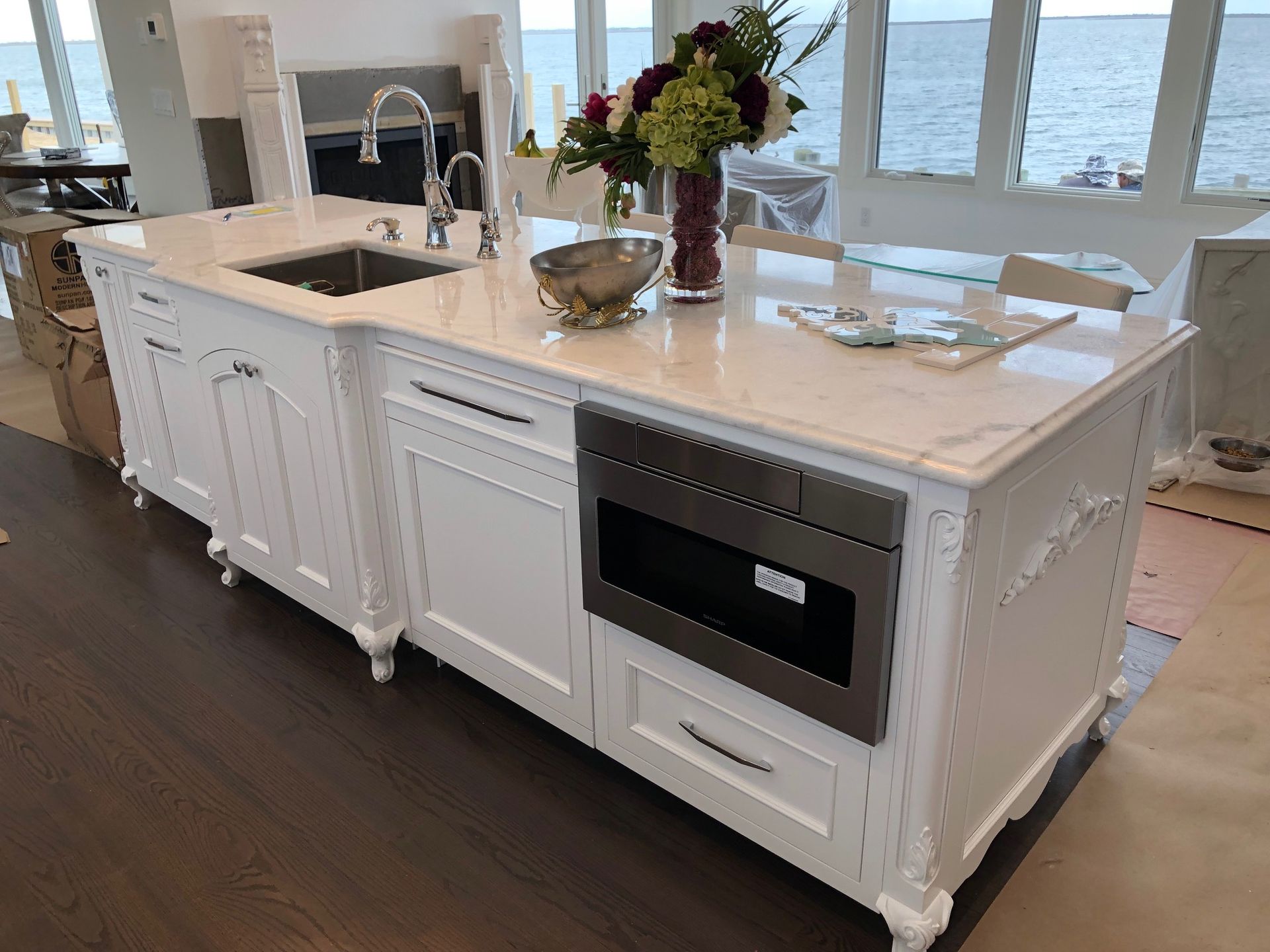 A large white kitchen island with a sink , microwave , and a vase of flowers.