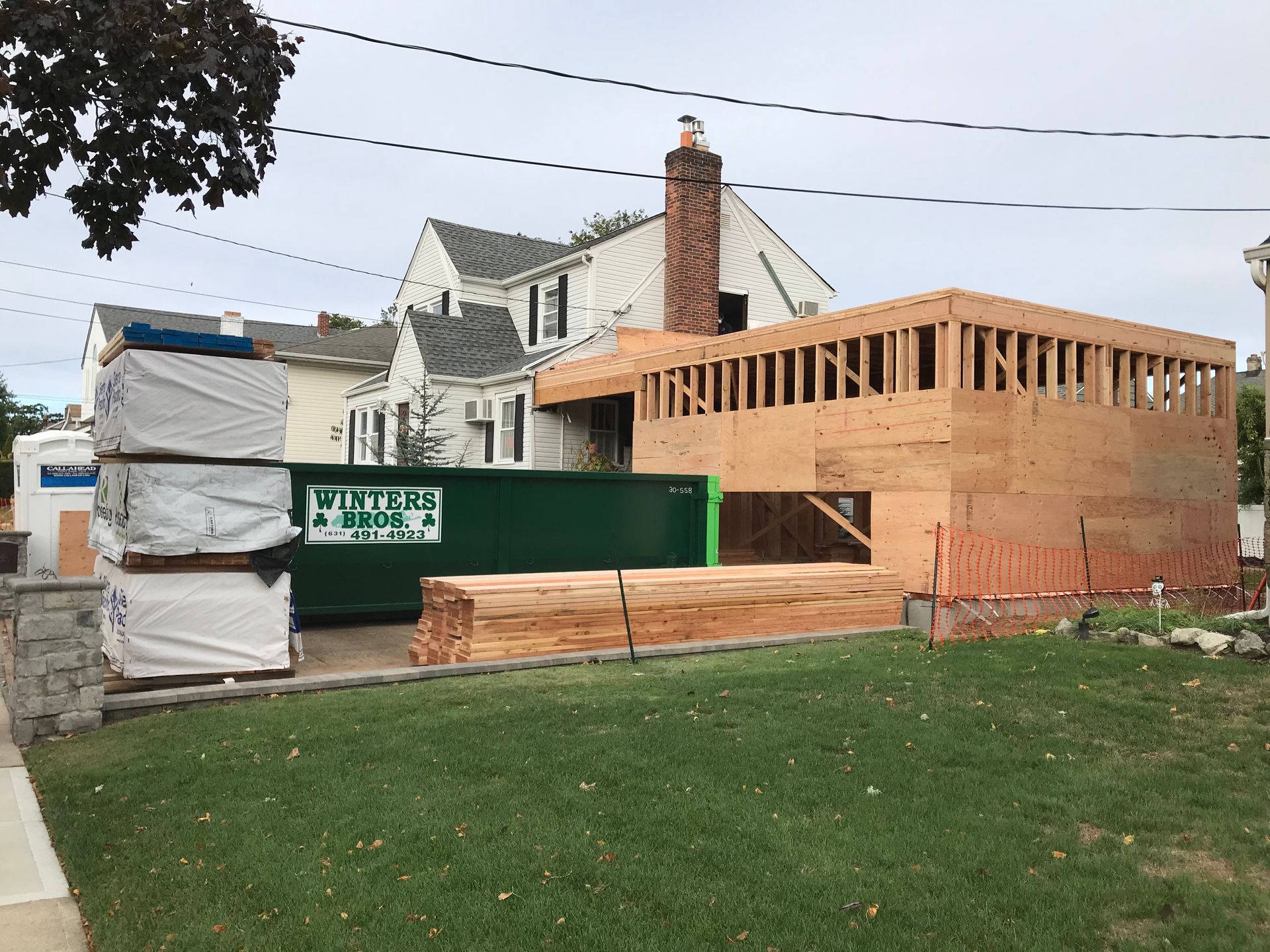 A green dumpster is sitting in front of a house under construction.