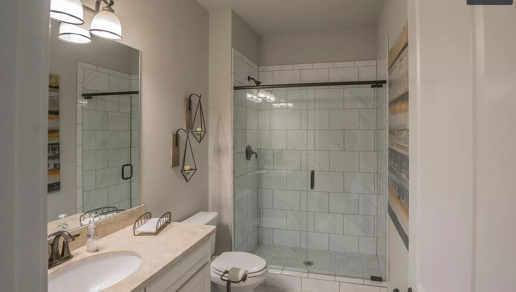A bathroom with a toilet , sink , mirror and walk in shower.