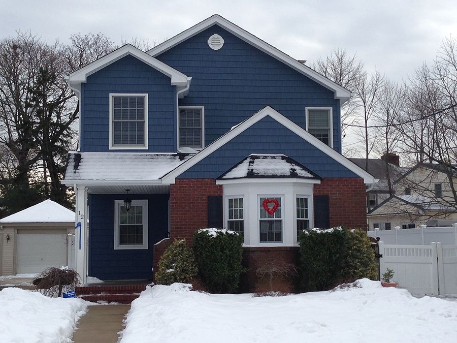 A blue house with white shutters and a red wreath on the front door