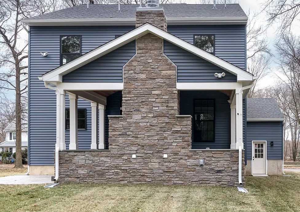 A blue house with a stone chimney on the front porch