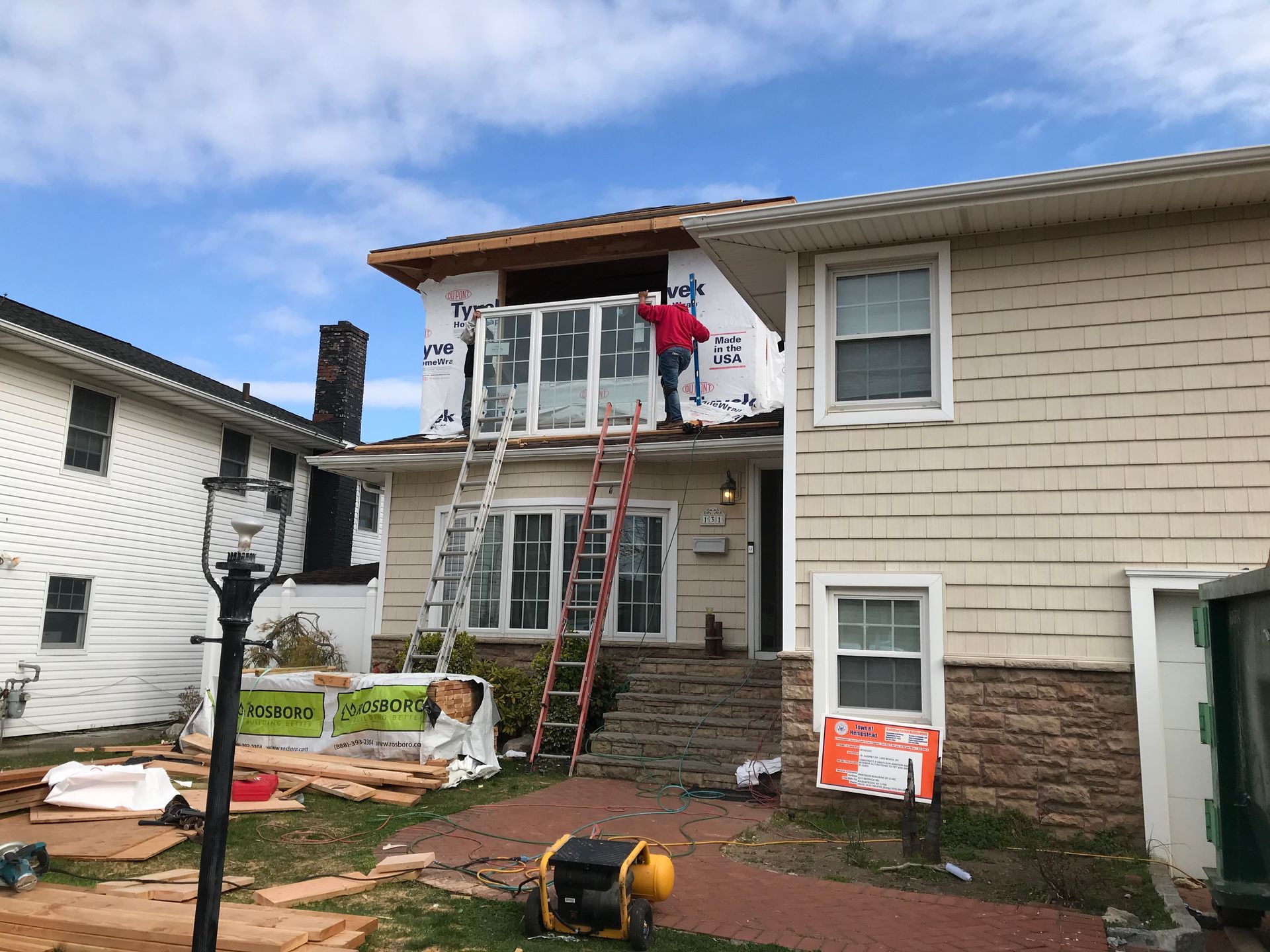 A man is standing on a ladder on the roof of a house.