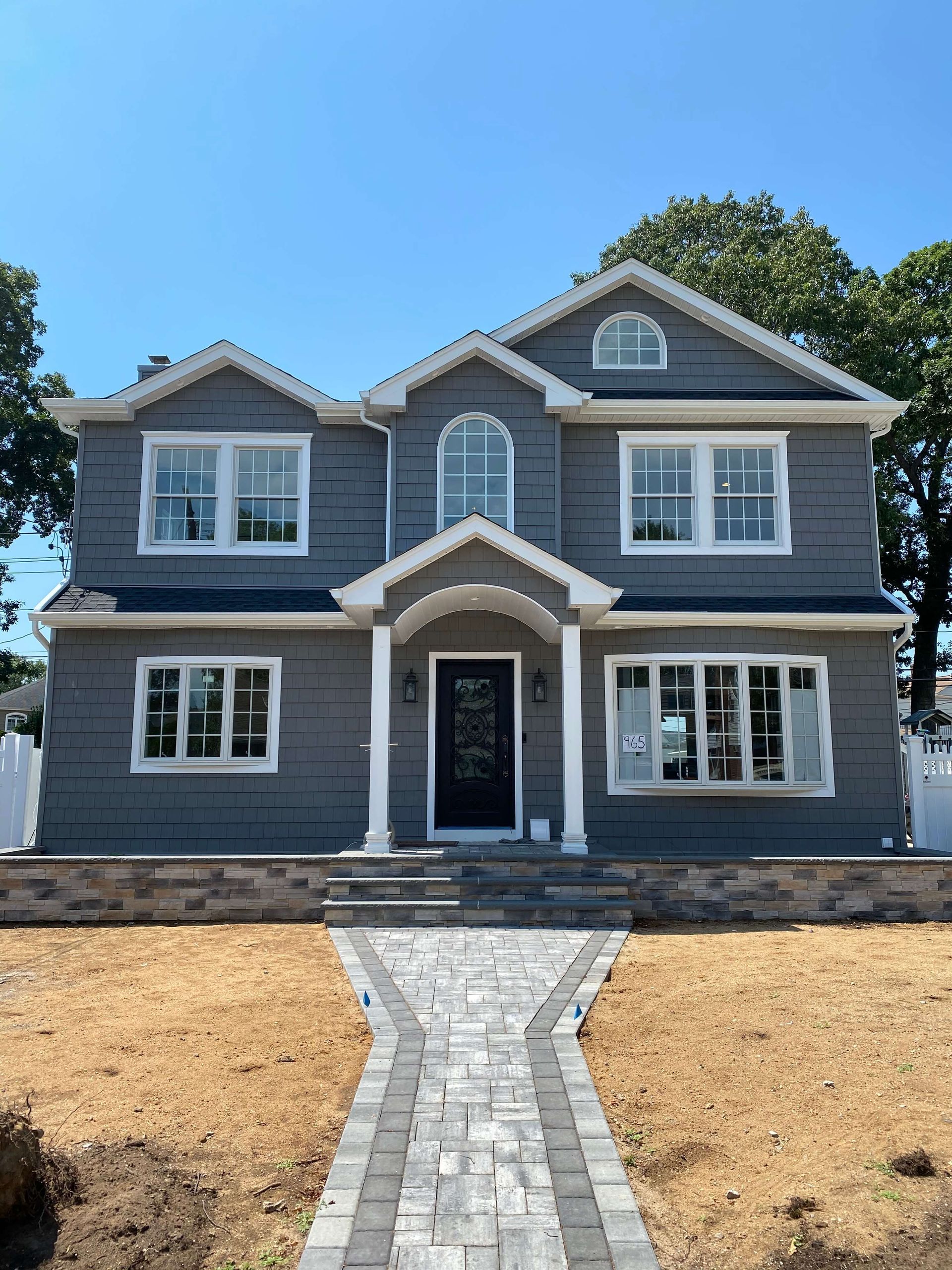 A large gray house with a brick walkway leading to it.