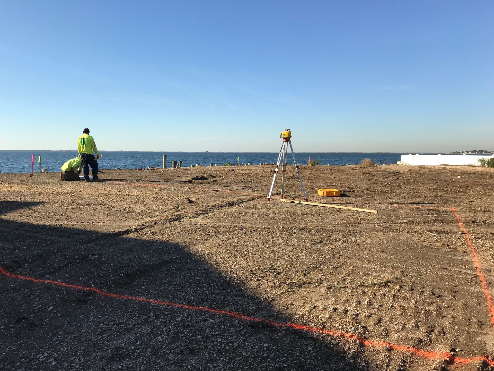 A group of construction workers are working on a dirt field near the ocean.