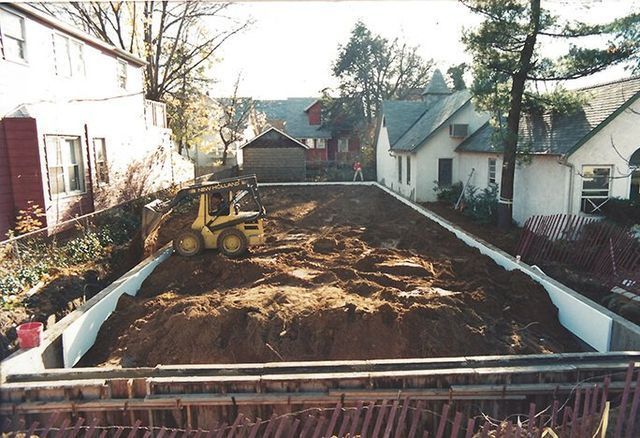 A yellow bulldozer is moving dirt in front of a row of houses