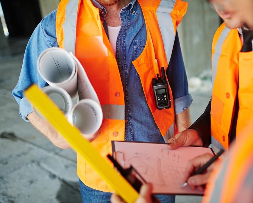 Two construction workers are looking at a clipboard and holding rolls of pipes.