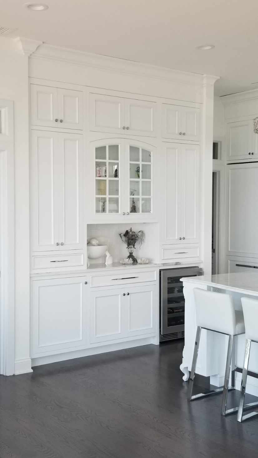 A kitchen with white cabinets , stools , and a refrigerator.