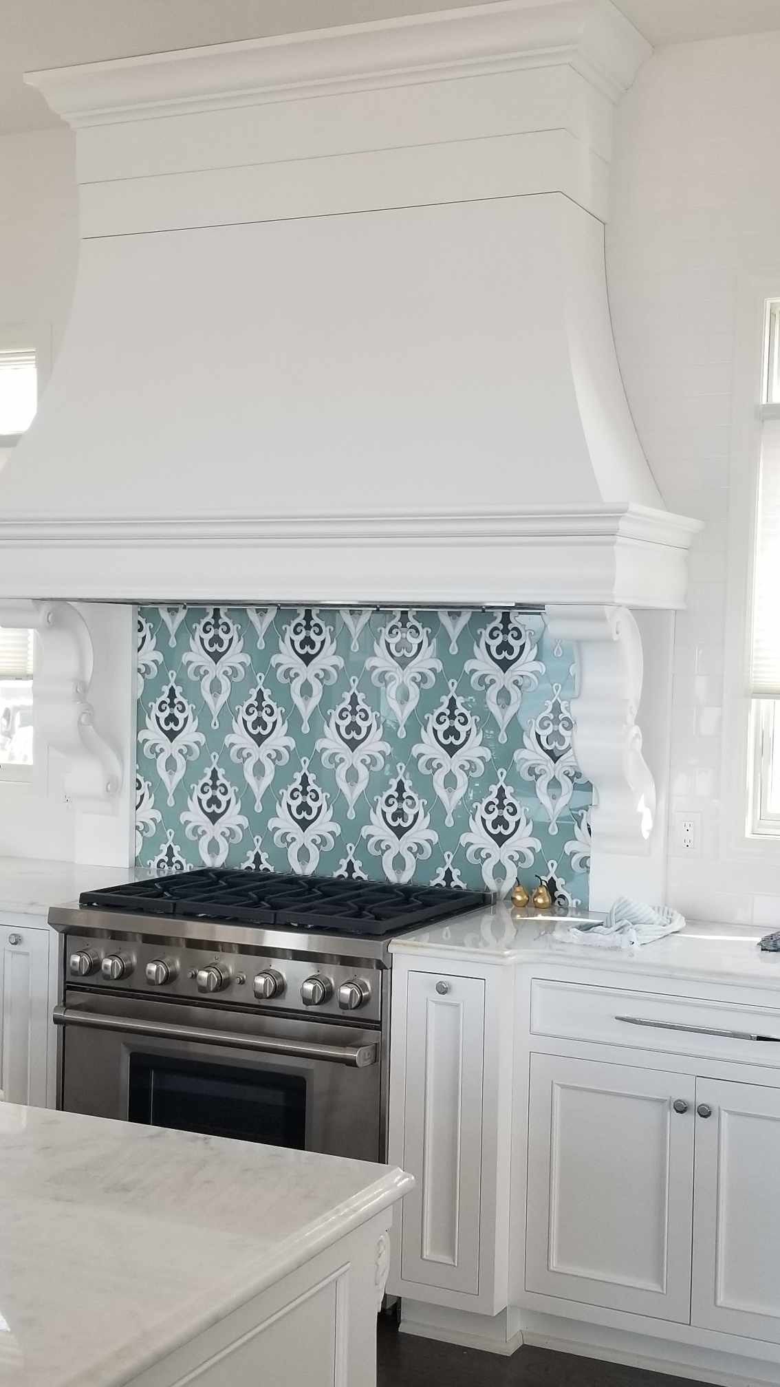 A kitchen with white cabinets , a stove , and a hood.