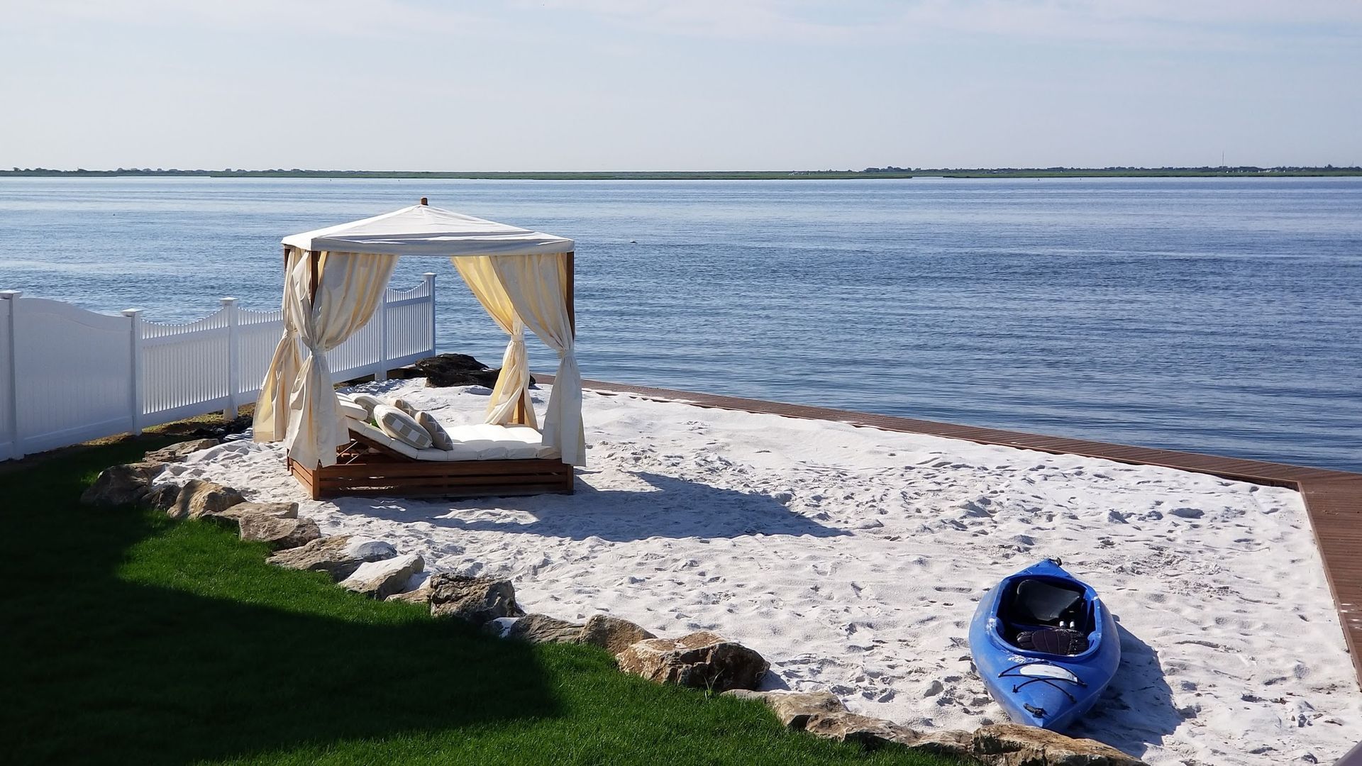 A canopy bed is sitting on a sandy beach next to a body of water.