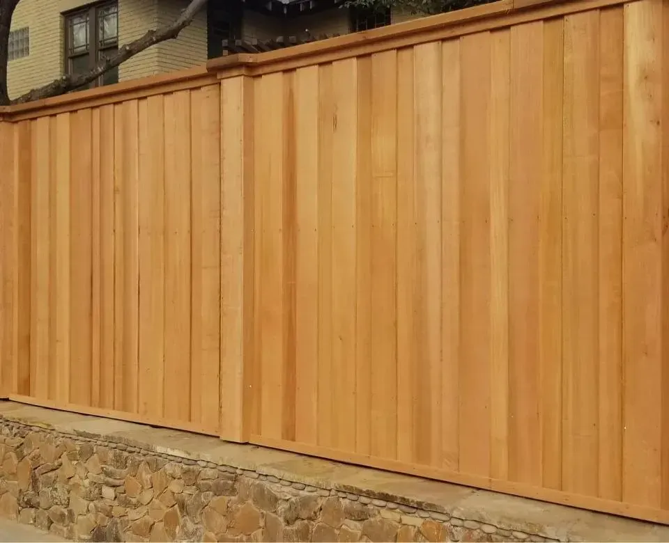 Wooden privacy fence atop a stone retaining wall beside a residential building