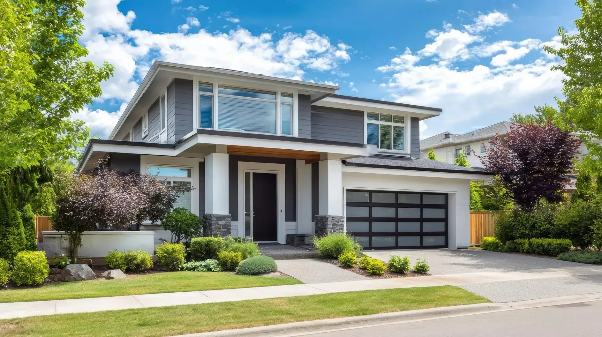 Modern two-story suburban house with a driveway, garage, and landscaped front yard under a blue sky