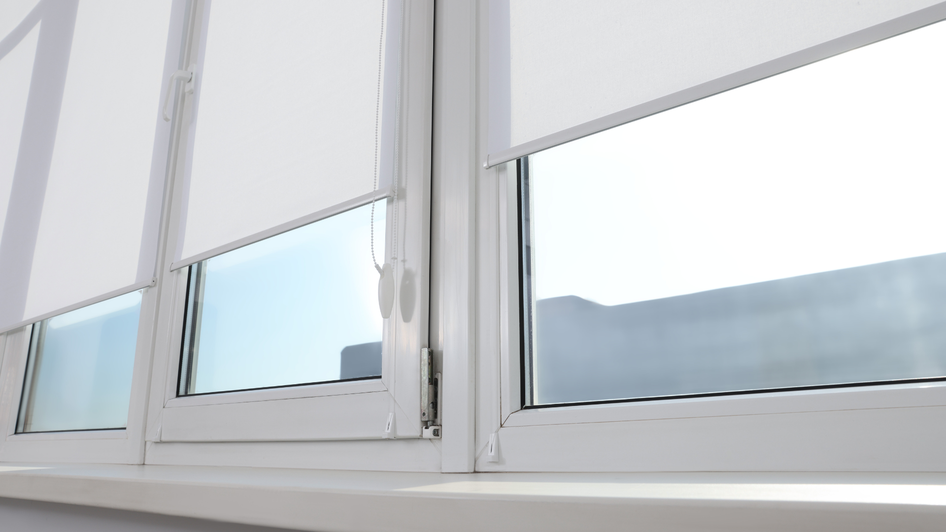 Three white windows with partially lowered white roller shades; bright outdoor view.