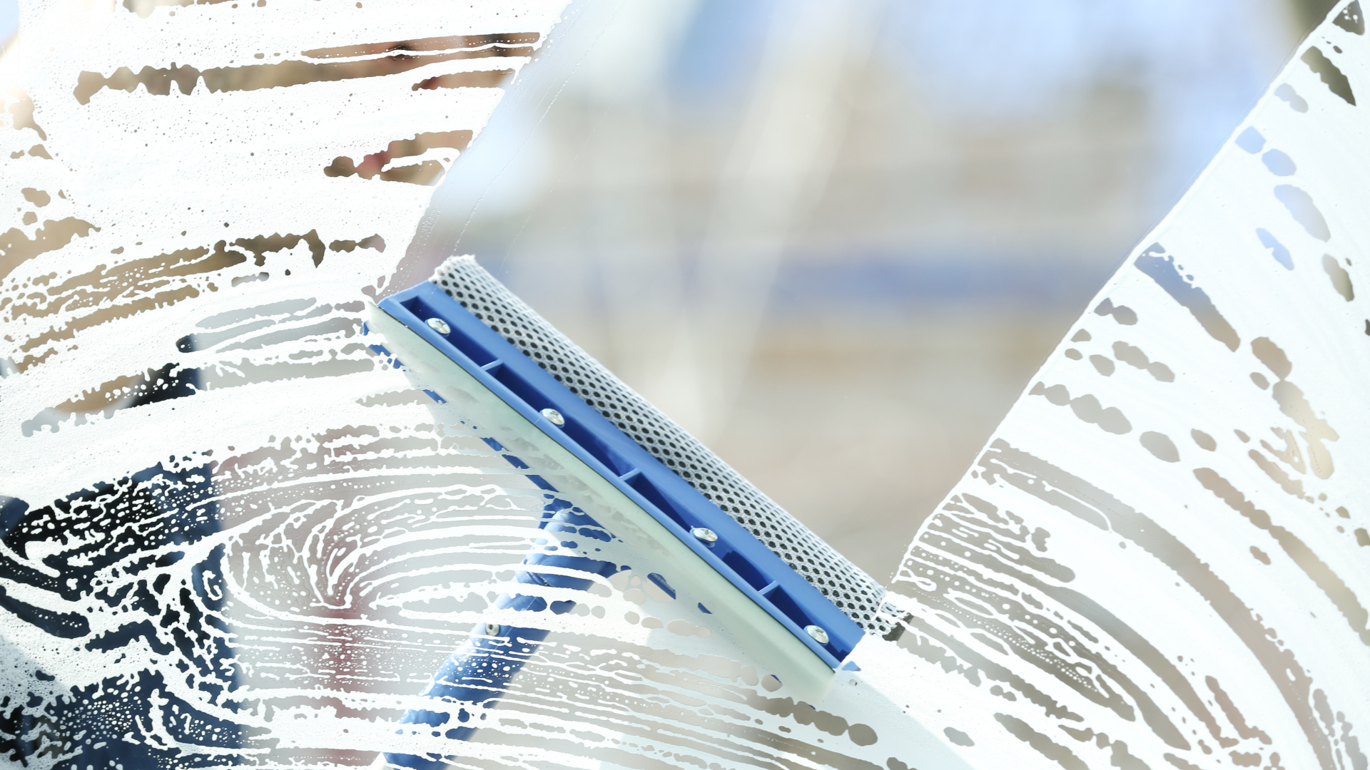 Window being cleaned with soapy water and a blue squeegee.