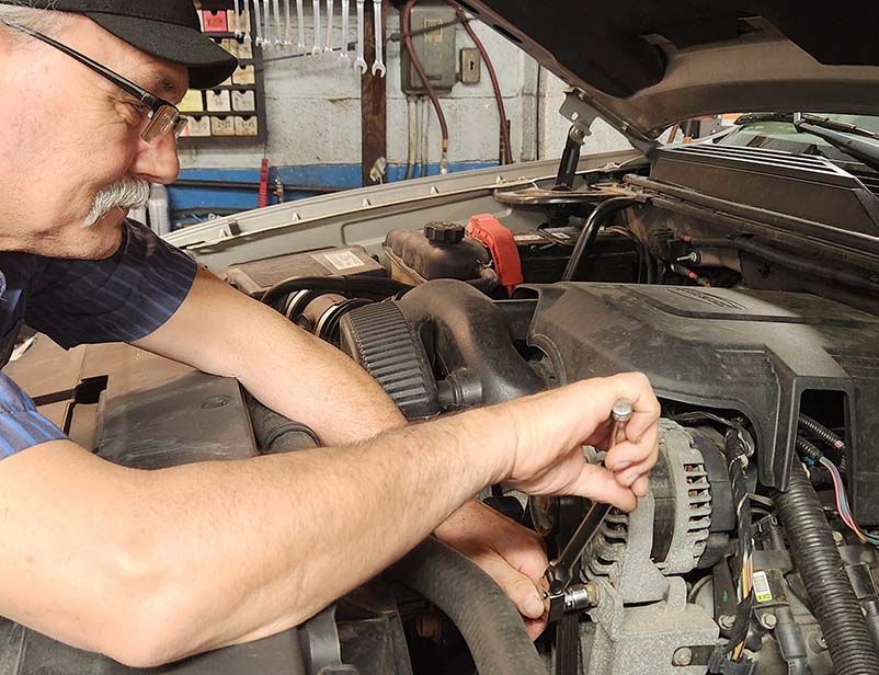 Mechanic working on a car engine, using a wrench inside a garage.